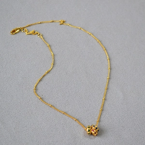 Détail d'un collier chaîne à billes dorée avec pendentif vintage et zircons colorés