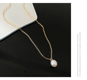 Close-up of a gold teardrop pearl necklace on a sleek black mirror surface