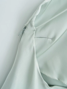 Close-up of invisible zipper detail on light green satin silk dress with smooth texture