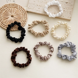 Flat lay of seven colorful satin scrunchies set on decorative coasters and stone plates