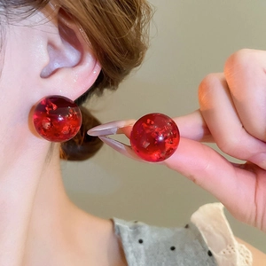Close-up of elegant red resin pearl earrings with glitter details on a model