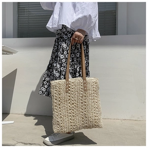 Detail of the woven texture and brown leather strap on a beige straw tote bag