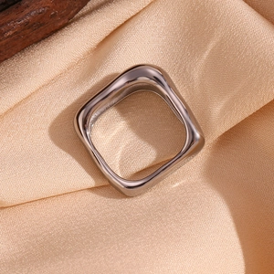 Bague géométrique carrée argentée minimaliste posée sur un tissu en soie beige doux