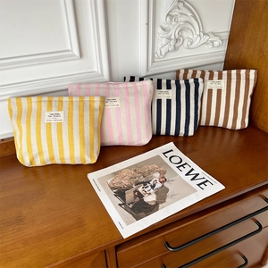 Striped woven cosmetic bags in four colors arranged on a wooden table with cotton linen texture