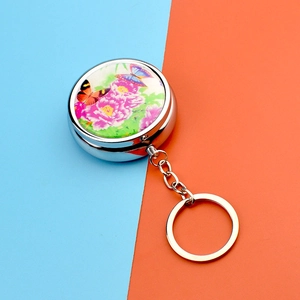 Detailed view of round metal pill box keychain with floral and butterfly pattern