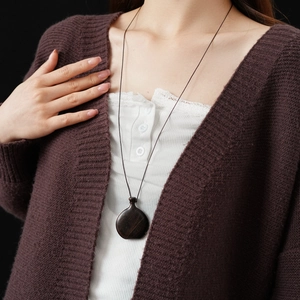 Close-up of a drop-shaped dark wood wine bag pendant necklace worn on a brown cardigan