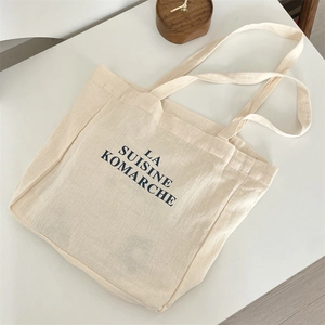 Detailed macro view of cream canvas tote bag featuring black French lettering and texture