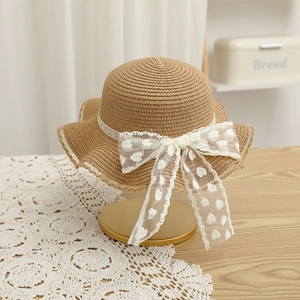 Détail d'un chapeau en paille enfant avec ruban en dentelle et nœud en tulle