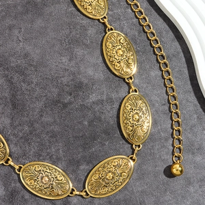 Detailed view of golden metal belt with oval floral embossed patterns and chain drop