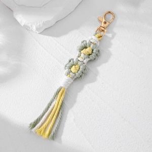 Close-up of handmade woven daisy flower keychain with sage green tassels and gold clasp