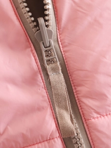 Detail van een beige ritssluiting op een roze gewatteerde bodywarmer voor dames