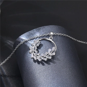Elegant silver leaf zircon necklace with a round pendant on a dark textured background