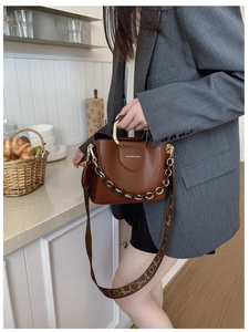 Brown bucket bag detail with gold metal handle and wide jacquard logo shoulder strap