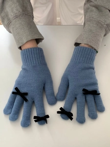 Close-up of blue knitted gloves with black bows on a clean white surface