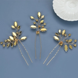 Detailed view of three gold bridal hair pins with crystal leaves on a blue background