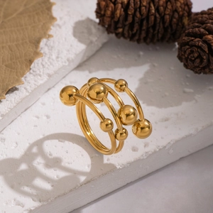 Macro shot of tiered gold-plated spiral ring with polished beads on stone surface