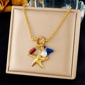 Detail van gouden zeester hanger met parel en blauwe kwast op een kralen ketting