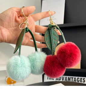 Detail of red and mint green cherry plush keychains with golden metal clasp and leather leaves