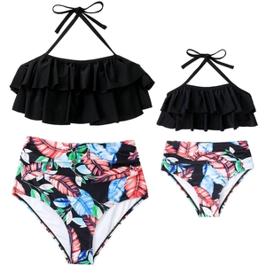 Flat lay of mother and daughter matching swimsuits with ruffled tops and tropical print bottoms