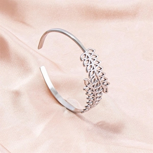 Macro shot of silver C-shaped steel bracelet with leaf design on pink satin