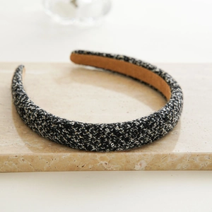 Detail of black and gold tweed headband on beige marble surface with soft lighting