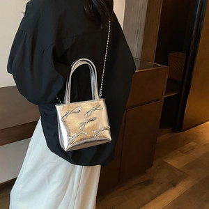 Minimalist silver bow purse with metallic finish and chain strap worn by a model
