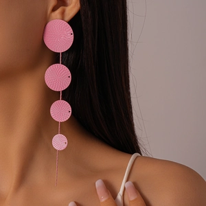 Close-up of pink long tassel earrings with textured circular disks on a fashion model