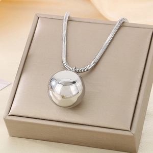 Detailed shot of a silver spherical pendant on a snake chain over a beige jewelry box