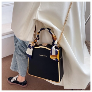 Detail of a chic black box bag with golden trim and silk scarf handle on a crossbody model
