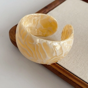 Close-up of wide open bangle featuring creamy yellow marble pattern and resin texture