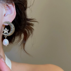 Macro detail of retro gold moon earring with star crystal and drop pearl on ear
