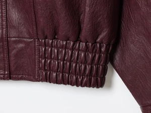 Detailed macro view of burgundy PU leather jacket hem with elasticated pleated texture