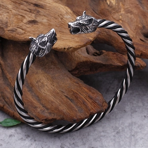 Close-up of a Norse wolf head torque bangle with twisted rope texture on a rustic wooden base