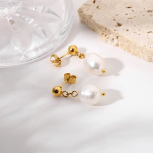 Detail showing elegant white baroque pearl drop earrings with golden stud and metal finish