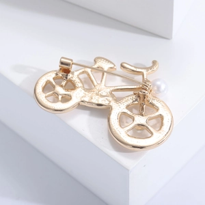 Macro detail showing the gold bicycle brooch's secure pin clasp and metal texture