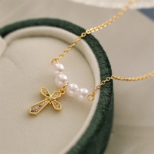 Close-up of golden cross pendant with colorful zircons and four white pearls on a fine chain
