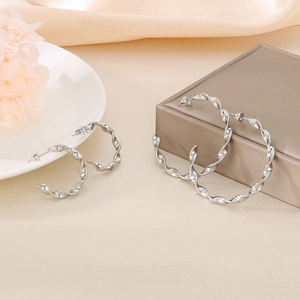 Minimalist twisted silver hoop earrings in large and small sizes on an elegant background