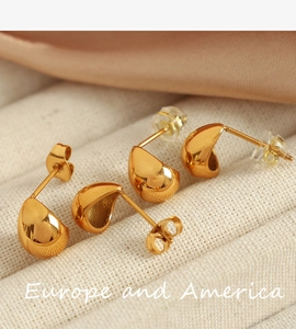 Macro shot of gold teardrop stud earrings on white textured fabric with silk accent