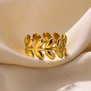 Polished gold stainless steel olive leaf ring on white silk fabric background
