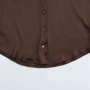 Détail d'un chemisier en satin marron montrant l'ourlet incurvé et les boutons dorés