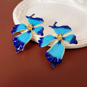 Macro detail of vintage blue enamel flower earrings with gold edges on white plate