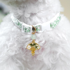 Close-up of pet collar with green leaf patterns and elegant fan-shaped charm on white fur
