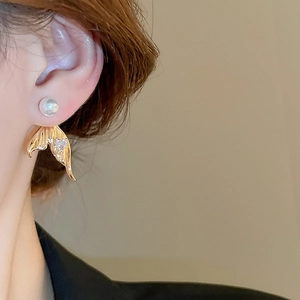 Close-up of elegant gold mermaid tail earrings with pearls and zircon on model's ear
