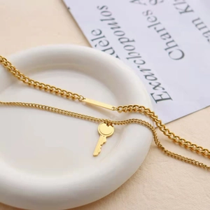Gold double-layer Cuban chain necklace with key pendant and bar on white ceramic plate