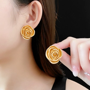 Close-up of vintage golden rose earrings worn by a model against a black background