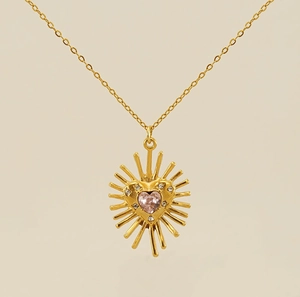 Détail du pendentif soleil doré avec zircon en forme de cœur rose et cristaux brillants