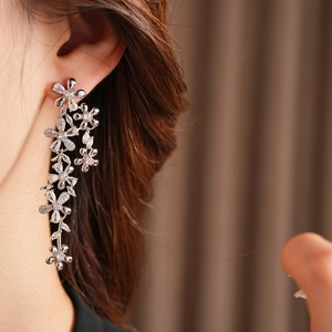Detailed view of silver tassel earrings with sparkling zircon flowers worn by a model