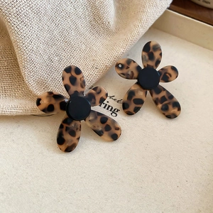 Detailed close-up of leopard print acetate flower earrings on a cream ceramic tray