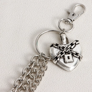 Detail of silver heart-shaped padlock charm with layered metal chains for trousers