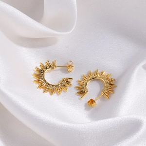 Macro view of gold sunburst spike earrings on white silk fabric with polished metal detail